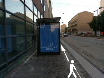 Šajā vietā taktilais bruģakmens ved tieši blakus reklāmas nojumei. Neredzīgs cilvēks var atdauzīt plecus pret nojumi.
