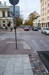 Šajā kadrā redzams jaunais (apakšā) un iepriekšējā gada (augšā) taktilā bruģa ieklāšanas veids. Iepriekš raupjais bruģis ieklāts ietves vidū, savukārt šogad ieklāts ietves malās.